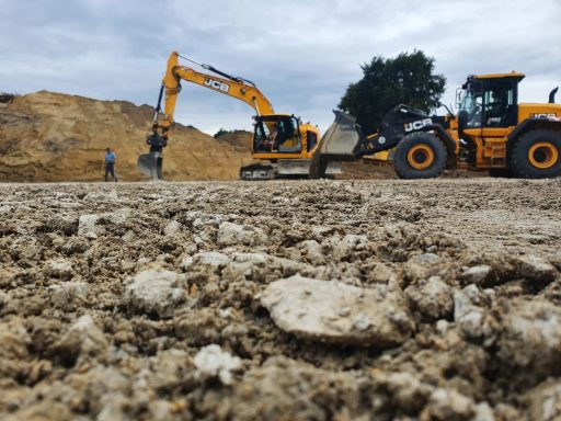 Baufahrzeuge arbeiten auf einer Erdbaustelle mit unebenem Boden und Wolken am Himmel.