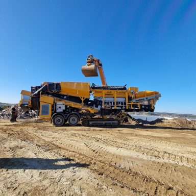Großes gelbes Baugerät mit Greifarm auf einer Baustelle unter klarem Himmel.