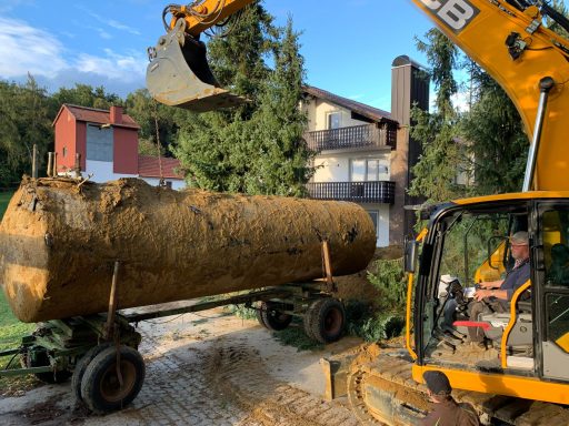 Bagger hebt großen, verschmutzten Tank vor Mehrfamilienhaus.