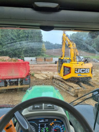 Blick aus einem Traktor auf Bauarbeiten mit einem Bagger und einem Lkw im Hintergrund.